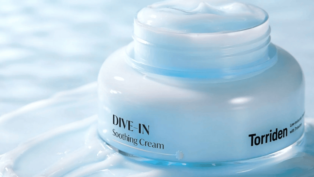 Närbild av en burk med "DIVE-IN Soothing Cream" från varumärket "Torriden", omgiven av en sval blå bakgrund och kräm.