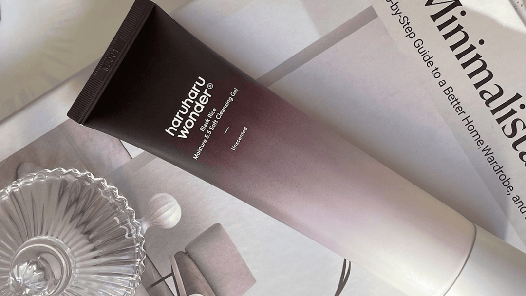 En mörkbrun tub med Haruharu Wonder Black Rice Soft Peeling Gel, liggande på en bok med texten "Minimalism" och en glasfat i bakgrunden.