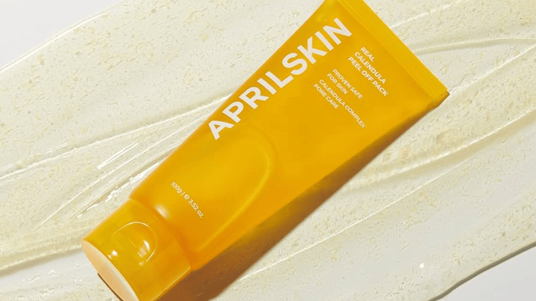 En tub av APRILSKIN Real Calendula Peel Off Pack ligger på en krämig texturyta, med fokus på den ljusa, energiska förpackningen.