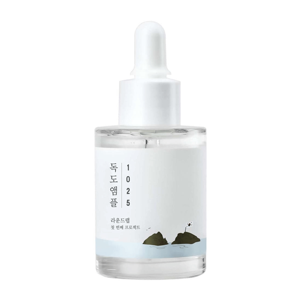 En gennemsigtig flaske med 1025 Dokdo Ampoule ansigtsserum, dekoreret med minimalistisk havtema, på hvid baggrund.