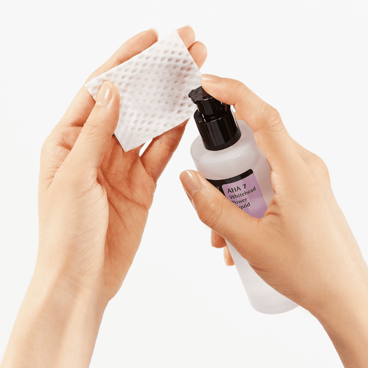 Påføring af COSRX AHA 7 Whitehead Power Liquid på bomuldspad, eksfolierende toner med AHA for at fjerne døde hudceller og forbedre hudstruktur.