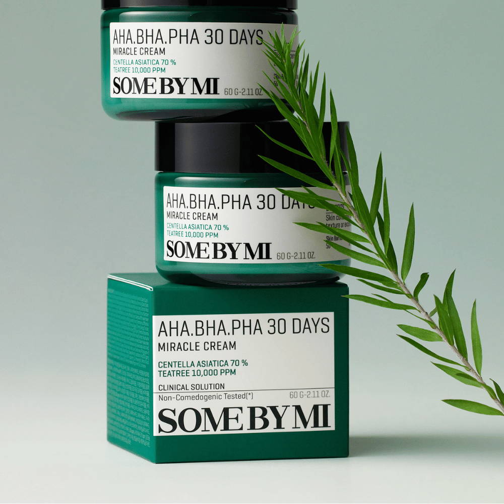 Et billede, der viser to krukker af "SOME BY MI AHA, BHA, PHA 30 Days Miracle Cream" stablet på en grøntonede plade. Cremen, som er rig på centella asiatica og tea tree-olie, er designet til at forbedre hudens kvalitet og lindre problemhud. Virker fugtgivende og beroligende.