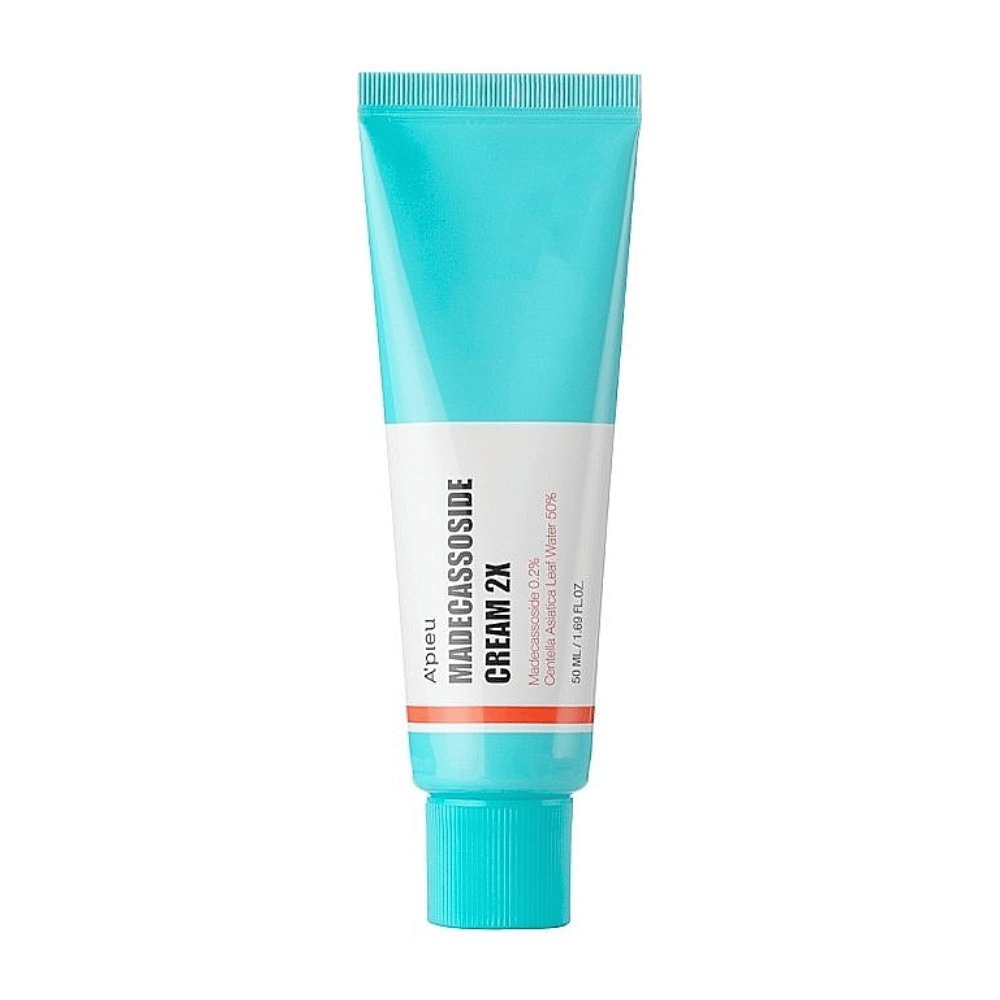 En tube med A'PIEU Madecassoside Cream 2X, med en lys turkis farve på toppen, der går over i hvid mod bunden. Tuben har tydelig tekst, der angiver mærke og produktnavn samt den aktive ingrediens Madecassoside 2%. En orange accentfarve går som en stribe rundt om tuben. Produktet ser ud til at være en hudcreme, der er rettet mod hudpleje og reparation. Baggrunden er neutral for at holde fokus på produktet.