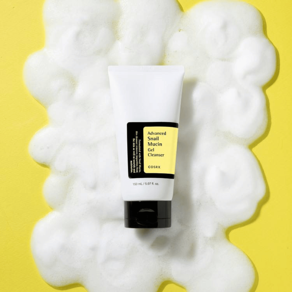 COSRX Advanced Snail Mucin Gel Cleanser 150 ml omgivet af rigeligt skum på gul baggrund – mild koreansk ansigtsrens med snail mucin for fugt og glans.