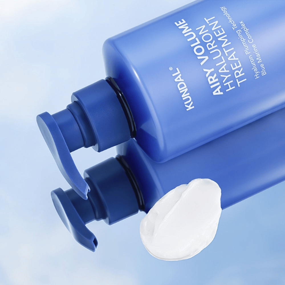KUNDAL Airy Volume Hyaluron Treatment i blå pumpeflaske liggende, med hvid cremeprodukt synlig ved siden af.