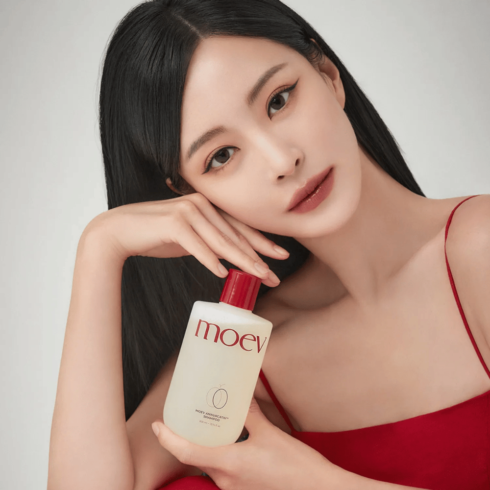 Kvinde med langt, glansfuldt hår holder MOEV Annurcatin Shampoo – en koreansk shampoo, der fugter, styrker og beskytter håret med naturlige ingredienser.