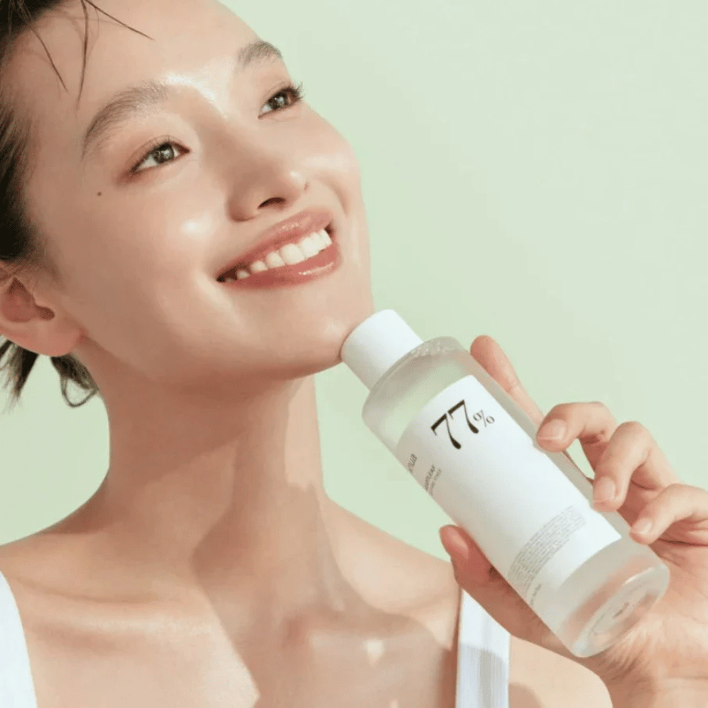 En kvinde beroliger sin følsomme hud med en flaske Heartleaf 77% Soothing Toner fra Anua, indeholdende kamæleonblad-ekstrakt.