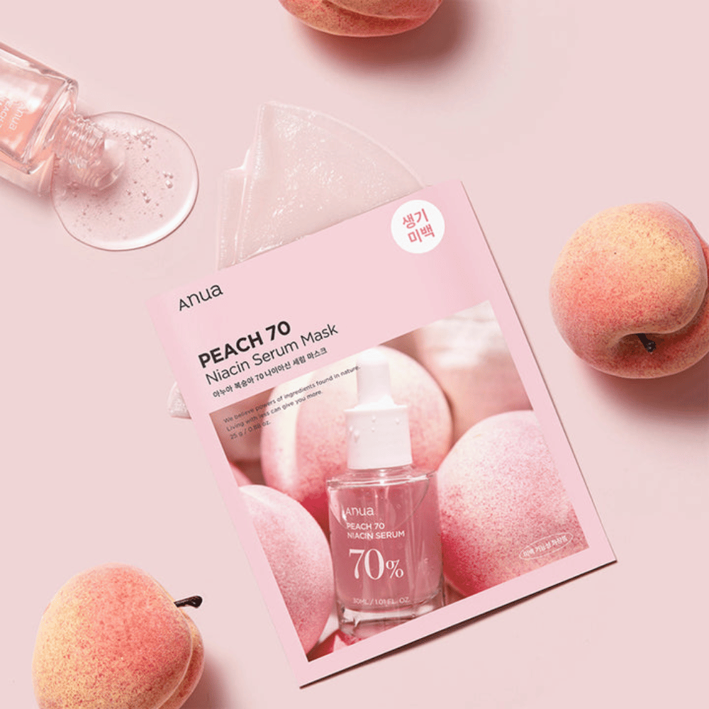 Et billede af Anua PEACH 70 Niacin Serum Mask, omgivet af ferskner og en flaske serum. Billedet har en blød lyserød baggrund, som komplementerer den lyserøde emballage og fremhæver produktet og ingredienserne.