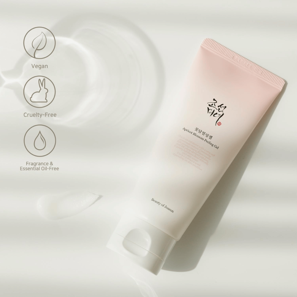 Et rør med Apricot Blossom Peeling Gel ligger på en reflekterende overflade med ikoner, der angiver, at produktet er vegansk, dyrevenligt og fri for duft og æteriske olier.