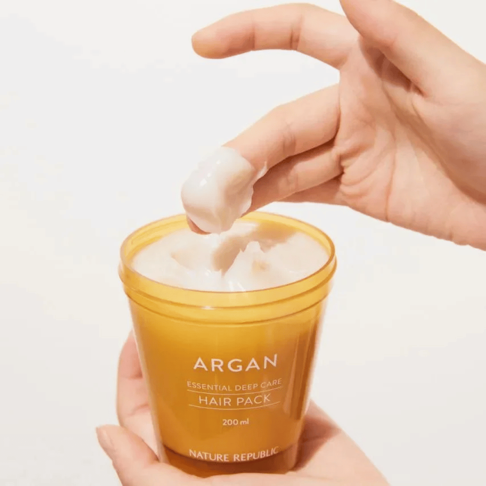 Hånd tager den cremede formel fra Nature Republic Argan Essential Moisture Repairing Hair Mask – intensiv næring til tørt hår.