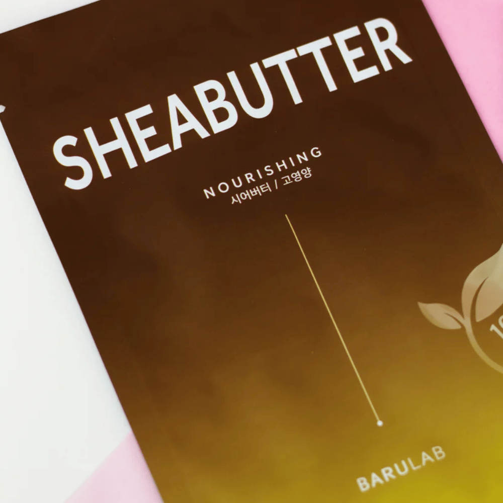 Et nærbillede af en pakke af BARULAB "SHEABUTTER Nourishing" maske. Produktet er mærket som "100% Vegan Product" og har en farvegradient fra mørkebrun til lysebrun.