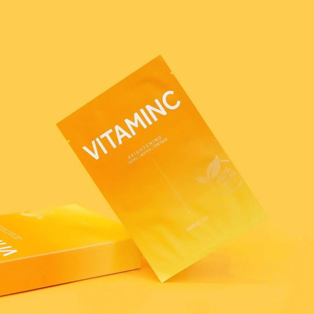 En bunke af pakker med BARULAB "VITAMINC Brightening" masker, alle mærket som "100% Vegan Product". Pakkerne har en farvetone i forskellige nuancer af orange og gul, placeret mod en ensartet gul baggrund.