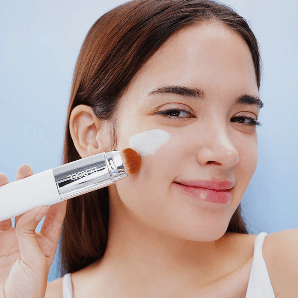 Model anvender ELROEL Blanc Cover Cream Stick concealer på kinden med indbygget børste for naturlig og jævn dækning.