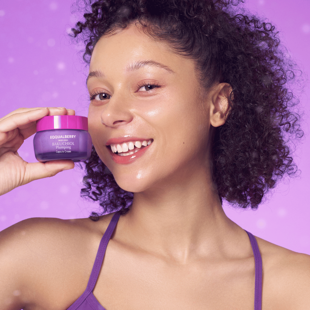 Kvinde med strålende hud holder EQQUALBERRY Bakuchiol Plumping Capsule Cream og smiler foran en lilla baggrund.