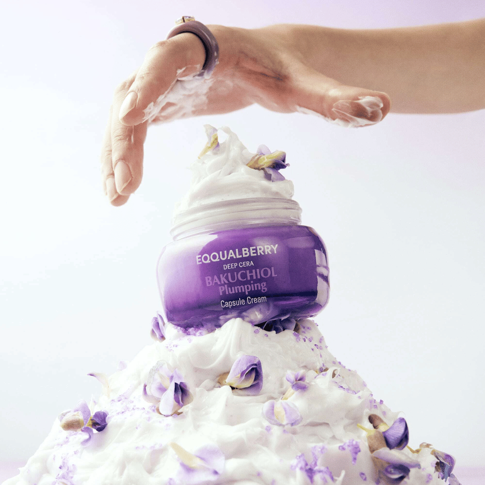 EQQUALBERRY Bakuchiol Plumping Capsule Cream placeret ovenpå en bunke af pisket creme med blomsterblade – symboliserer fugt og pleje.