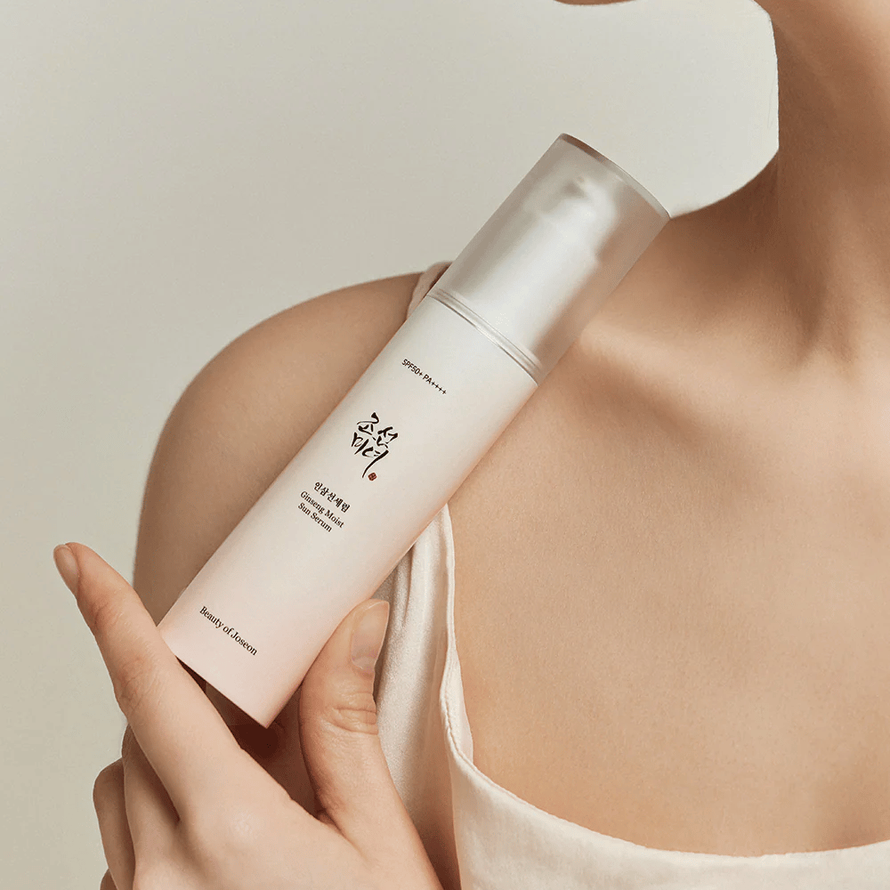 En kvinde, der holder en flaske Beauty of Joseon's Ginseng Moist Sun Serum SPF 50+ PA++++, som giver SPF 50+ PA++++ beskyttelse og hudplejefordele.