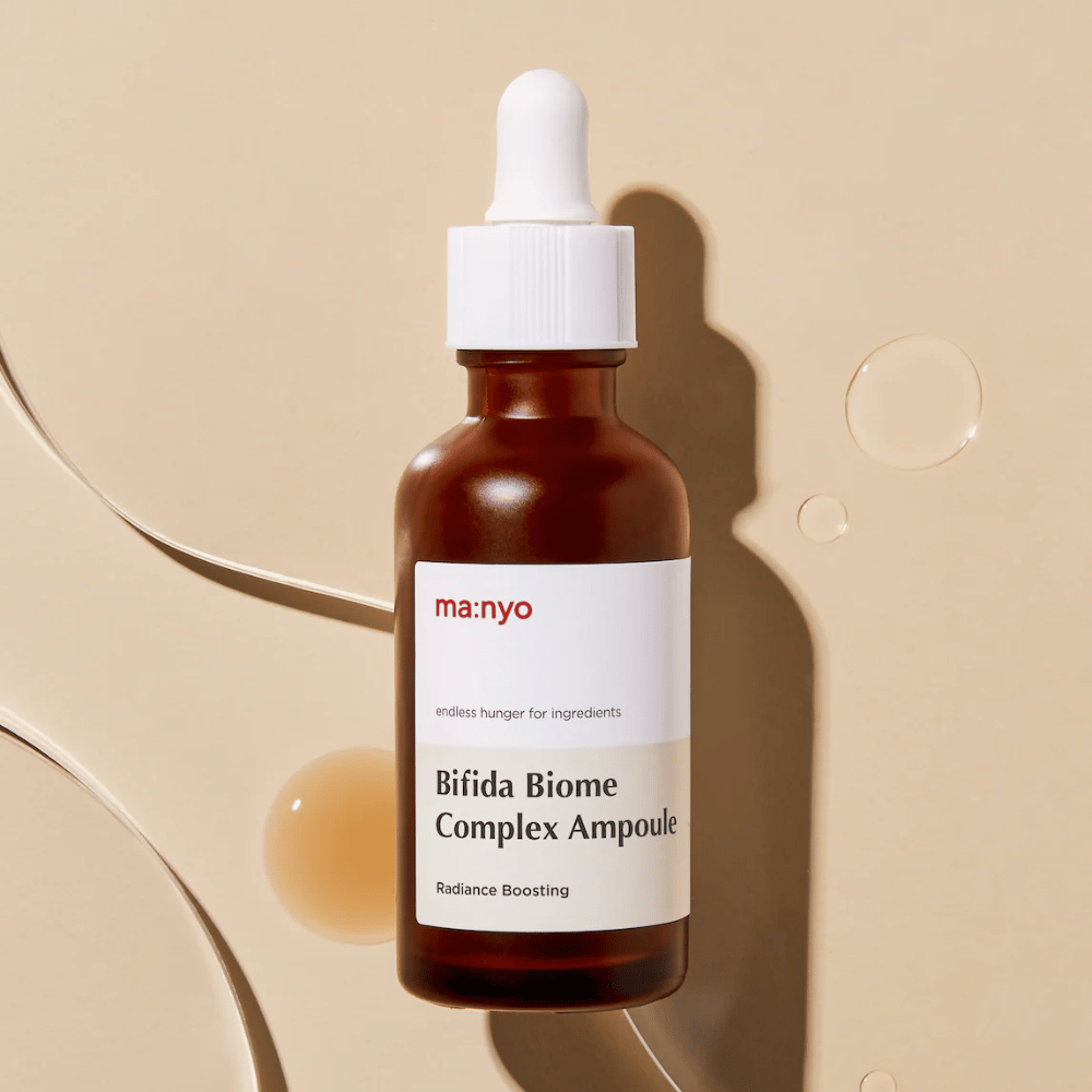 Stilrent produktbillede af ma:nyo Bifida Biome Complex Ampoule med fokus på flaskedesign og serumdråber i baggrunden.