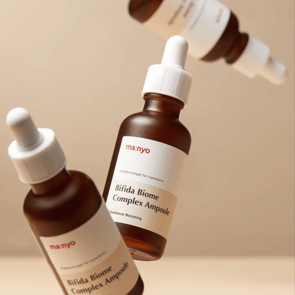 Produktbillede med flere svævende flasker af ma:nyo Bifida Biome Complex Ampoule mod beige baggrund, som giver en moderne og minimalistisk følelse.