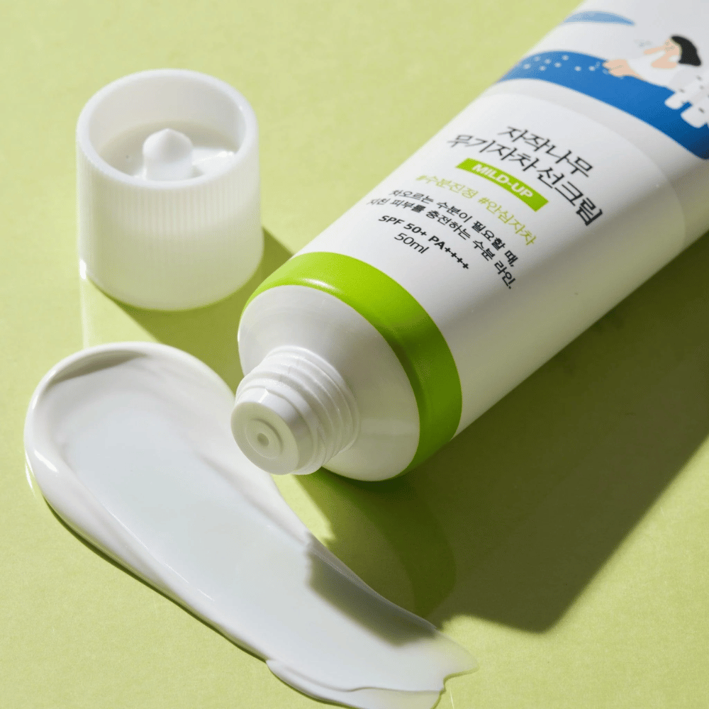Nærbillede af Birch Juice Moisturizing Mild Up Sunscreen med afskruet låg, hvid solcreme udsmurt på lysegrøn baggrund, SPF 50+ PA++++, 50 ml.