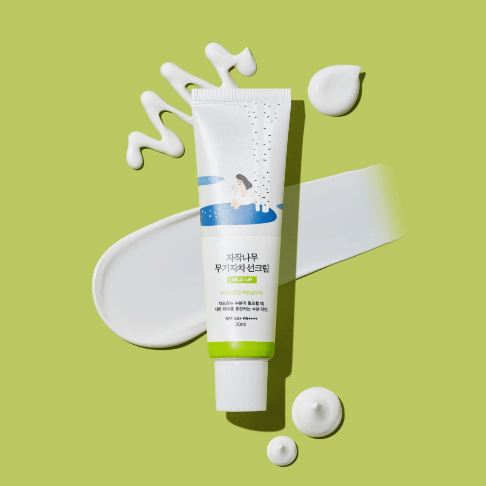 Birch Juice Moisturizing Mild Up Sunscreen – hvid tube med grøn base på grøn baggrund, omgivet af udsmurt solcreme og dråber, SPF 50+ PA++++, 50 ml.