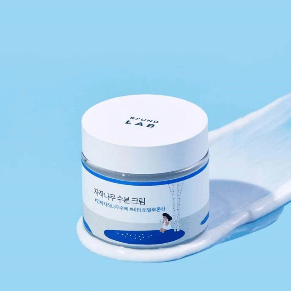 Round Lab Birch Juice Moisturizing Cream i blåtonet krukke med hvidt låg, stående i et lag af creme mod blå baggrund.