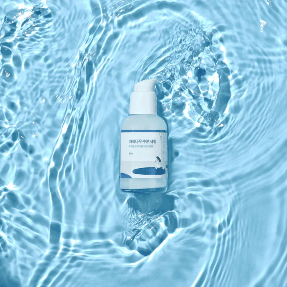 Round Lab Birch Juice Moisturizing Serum i pumpeflaske flydende på blåt vand med sollysreflektioner.