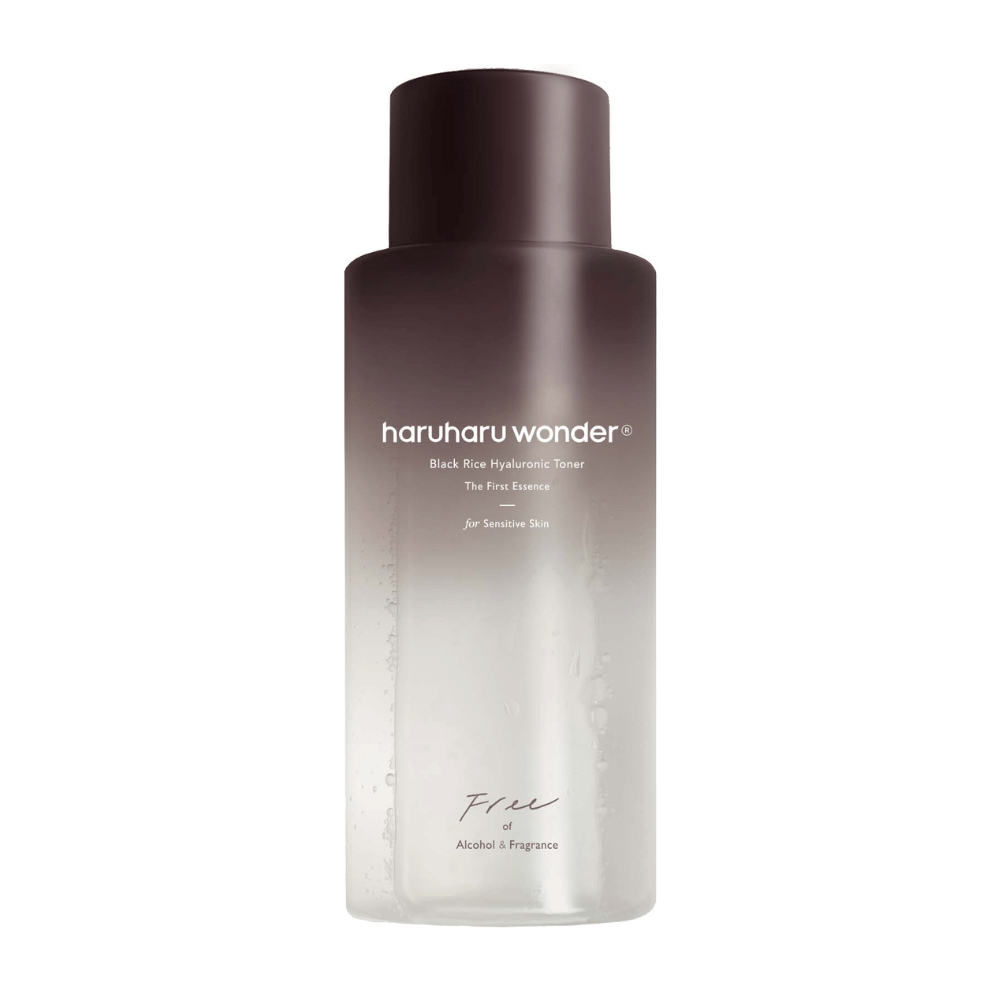 En flaske af haruharu wonder Black Rice Hyaluronic Toner The First Essence, med mørkebrun til gennemsigtig gradient og teksten "Free of Alcohol & Fragrance", på hvid baggrund.