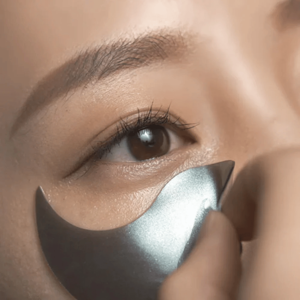Detaljeret billede, hvor en sort hydrogel eye patch påføres under øjet. Billedet viser den tætte pasform og den kølende følelse omkring øjenområdet.