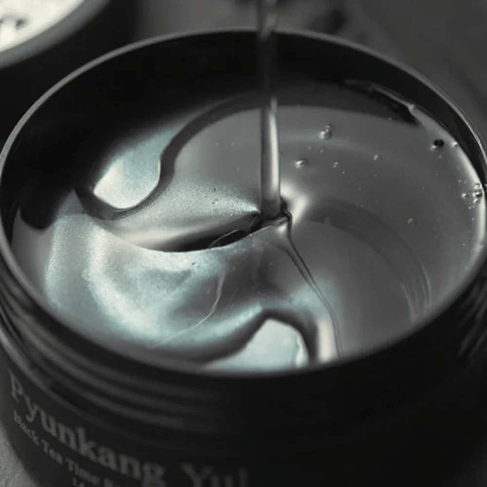 Nærbillede af sorte hydrogel eye patches i en åben krukke fra Pyunkang Yul. De glansfulde patches ligger i serum og fremhæver produktets fugtgivende og eksklusive følelse.