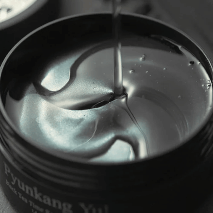 Nærbillede af sorte hydrogel eye patches i en åben krukke fra Pyunkang Yul. De glansfulde patches ligger i serum og fremhæver produktets fugtgivende og eksklusive følelse.