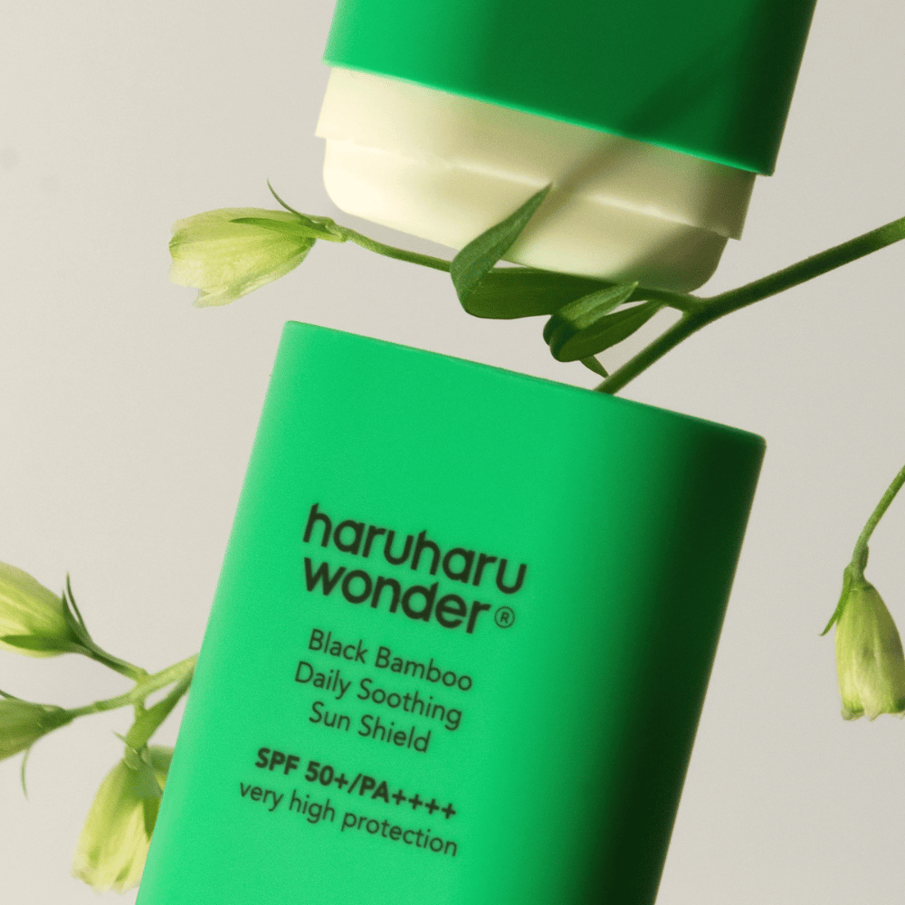 Nærbillede af Haruharu Wonder Black Bamboo Daily Soothing Sun Shield – en grøn solcreme i stiftformat med SPF 50+ PA++++, omgivet af grønne plantedele.
