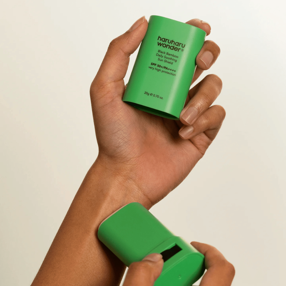 En person påfører Haruharu Wonder Black Bamboo Daily Soothing Sun Shield – en grøn solcremestick med SPF 50+ PA++++ – på håndleddet.