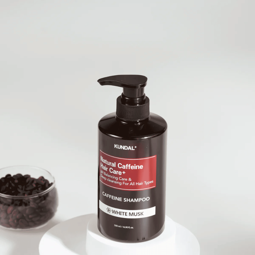 KUNDAL Natural Caffeine Hair Care+ Shampoo White Musk i sort pumpeflaske, 500 ml, placeret ved siden af en skål med kaffebønner.