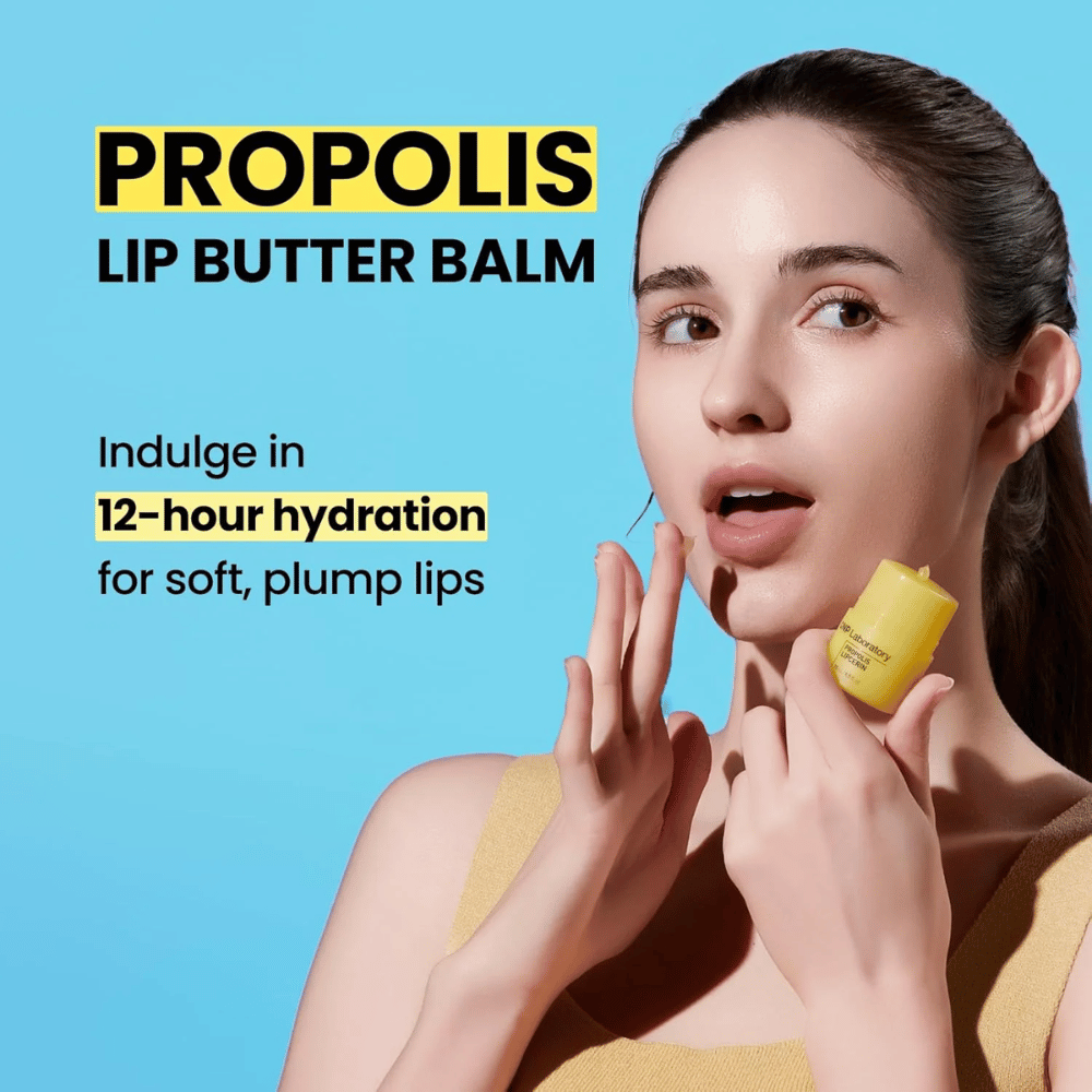 En kvinde påfører CNP Laboratory Propolis Lip Butter Balm, fremhævet mod en blå baggrund. Produktet lover 12 timers fugt til bløde og fyldige læber, hvilket vises med en gul tube hun holder i hånden.