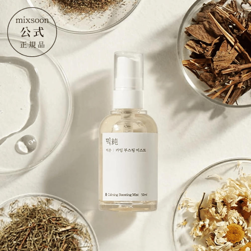 En gennemsigtig sprayflaske med etiketten 'Calming Boosting Mist' fra Mixsoon, omgivet af tørrede urter og blomster på hvide skåle mod en beige baggrund, hvilket fremhæver produkternes naturlige ingredienser.