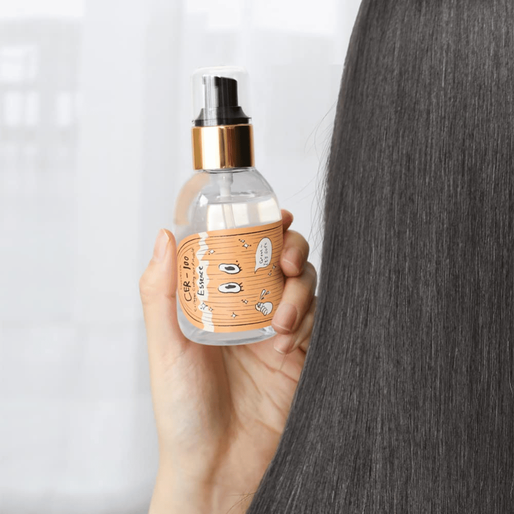 En person holder CER-100 Hair Essence ved siden af langt, glansfuldt hår for at vise blødhed og pleje.