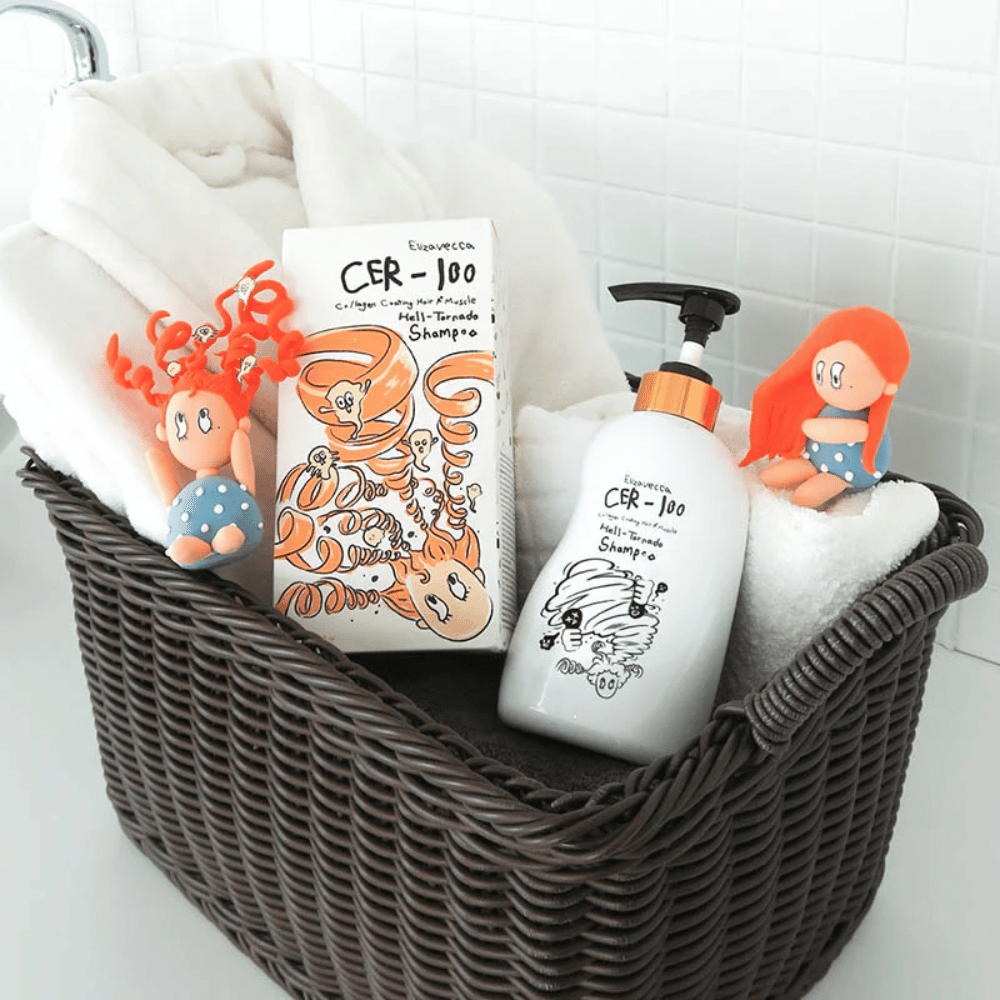 Præsentationsbillede med Elizavecca CER-100 Shampoo og produktemballage placeret i en kurv sammen med håndklæder. Legende figurer fra emballagedesignet fremhæver brandets unikke og kreative stil.