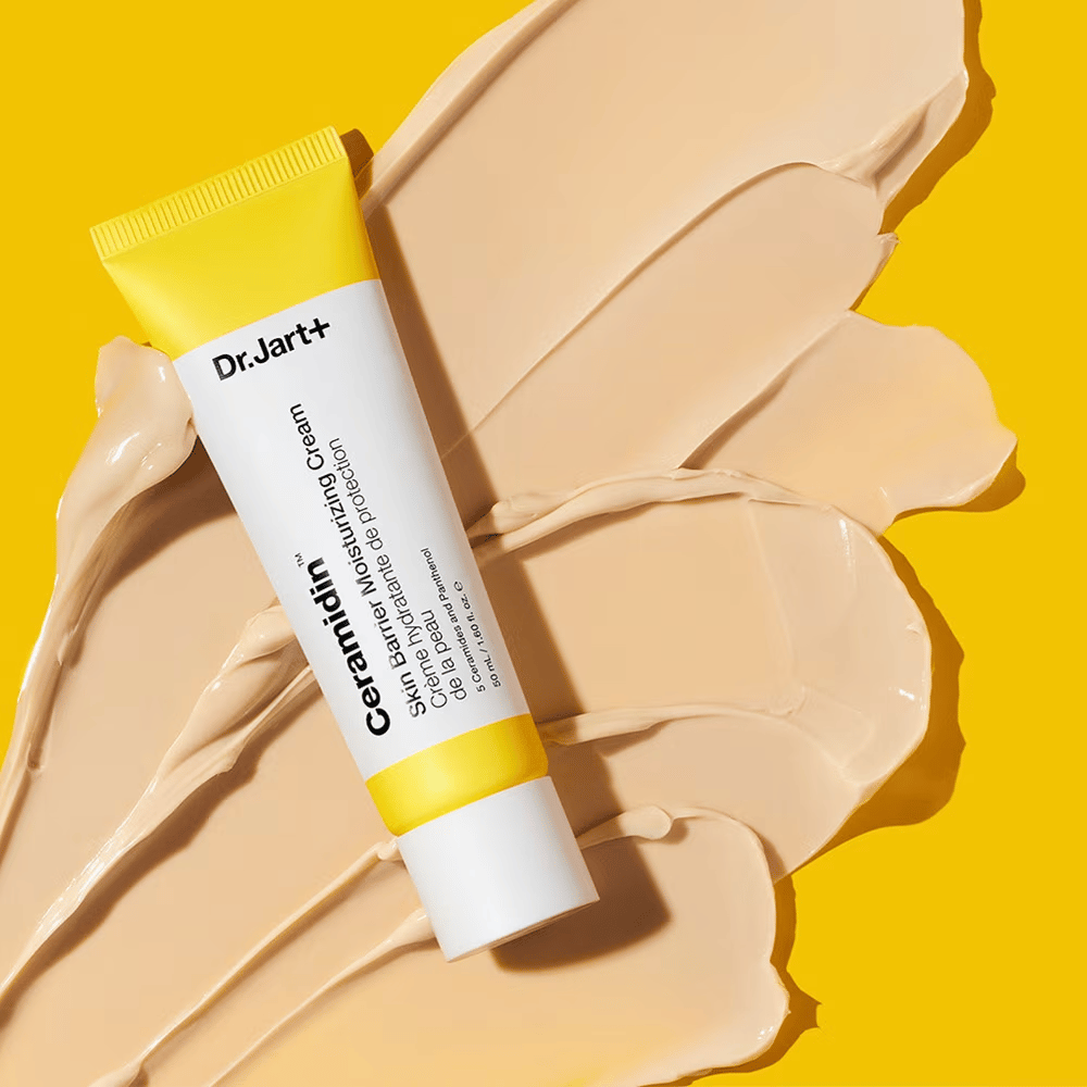 Tube med Dr. Jart+ Ceramidin Skin Barrier Moisturizing Cream mod en gul baggrund med creme spredt ud.