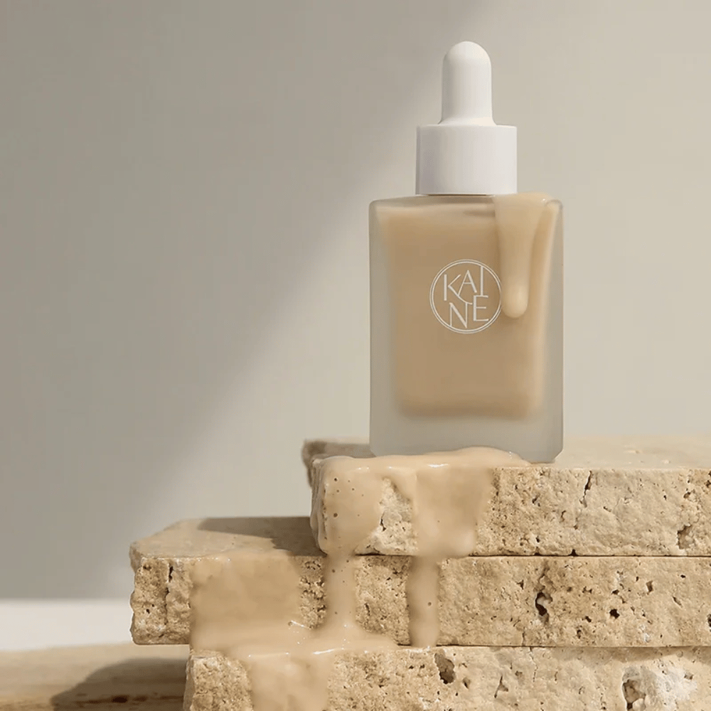 KANE Chaga Collagen Charging Serum i en frostet glasflaske med pipette. Cremet tekstur løber ned over naturlige sten i et blødt og minimalistisk lys.