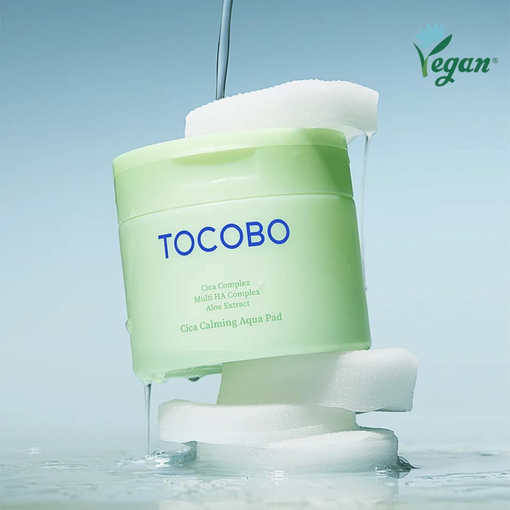 TOCOBO Cica Calming Aqua Pad placeret mellem toner pads med flydende essence. Vegan-symbolet understreger produktets veganske formulering og hudvenlige profil.