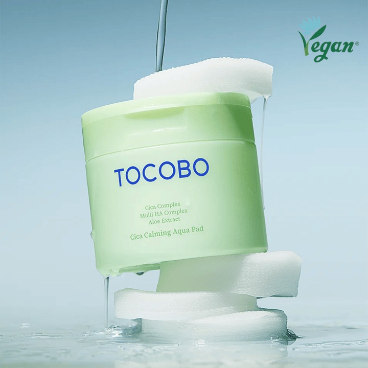 TOCOBO Cica Calming Aqua Pad placeret mellem toner pads med flydende essence. Vegan-symbolet understreger produktets veganske formulering og hudvenlige profil.