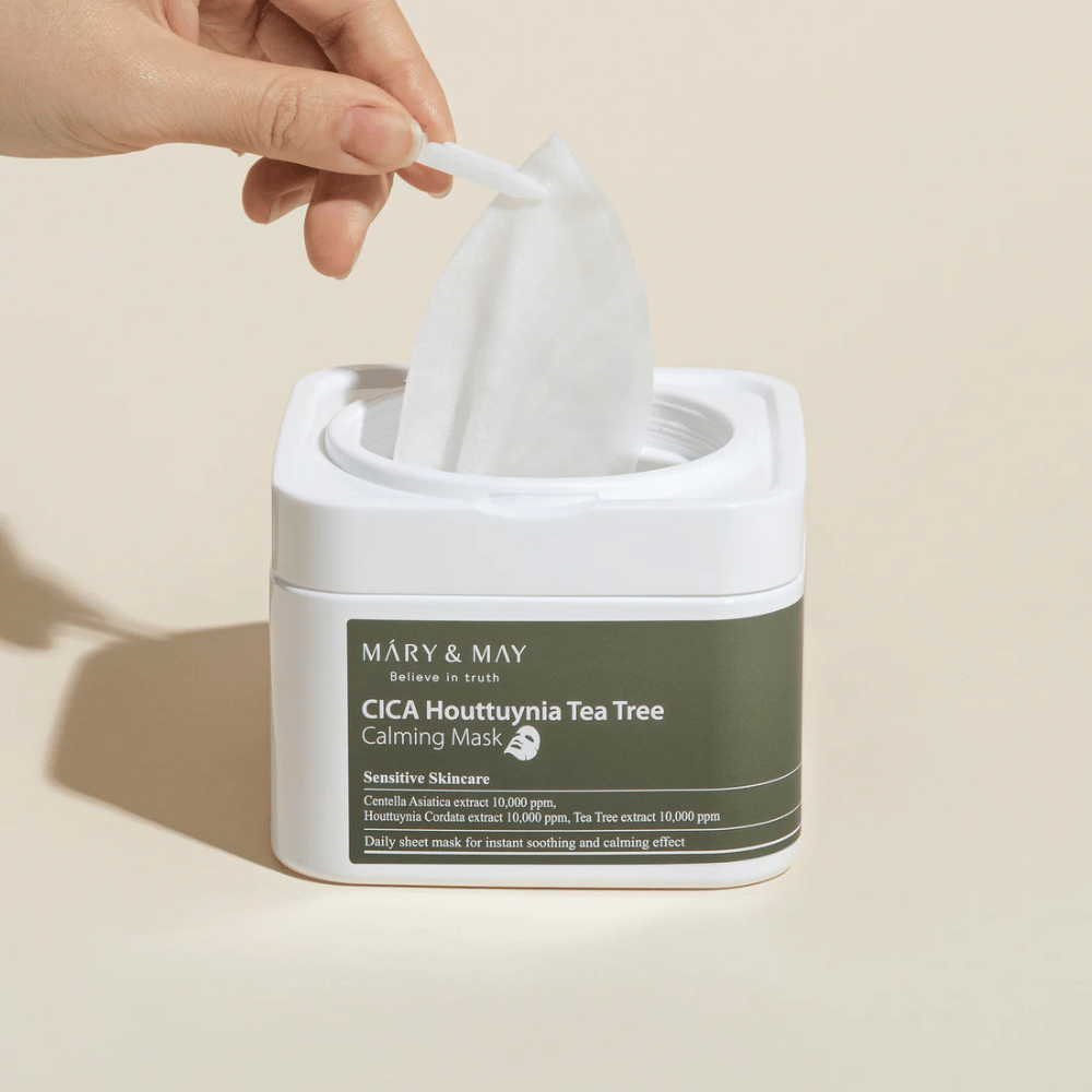 Hånd der trækker en sheetmaske op fra Mary & May Cica Houttuynia Tea Tree Calming Mask-krukke – beroligende ansigtsmaske til sensitiv hud med Cica og Tea Tree-ekstrakt.