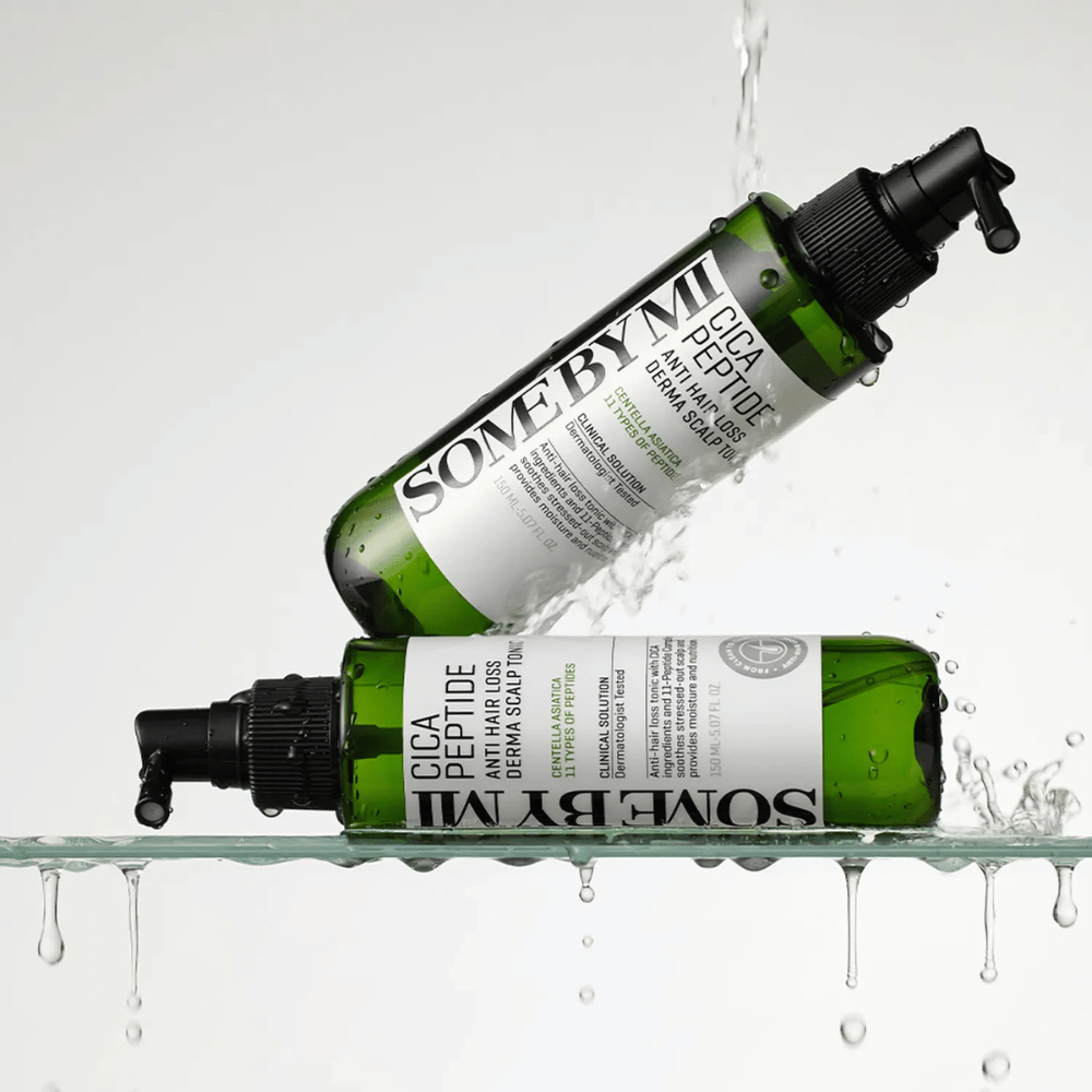 To flasker SOME BY MI Cica Peptide Anti Hair Loss Derma Scalp Tonic ligger i og over vand med dråber, der sprøjter, grønne flasker med sort spraymundstykke og hvid etiket.