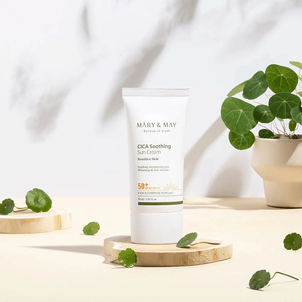 Mary&May CICA Soothing Sun Cream placeret på et træpodie med grønne centella-blade omkring. Billedet understreger de hudberoligende ingredienser og den naturlige inspiration bag produktet.