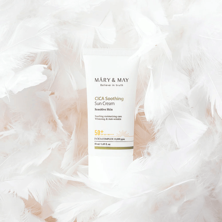Mary&May CICA Soothing Sun Cream omgivet af bløde hvide fjer. Billedet formidler en følelse af skånsomhed, komfort og let formel tilpasset sensitiv hud.