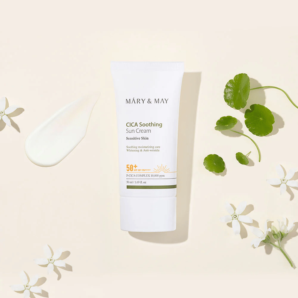 Mary&May CICA Soothing Sun Cream SPF50+ PA++++ præsenteret sammen med en cremetekstur, centella-blade og hvide blomster. Billedet fremhæver produktets beroligende egenskaber og fokus på sensitiv hud.