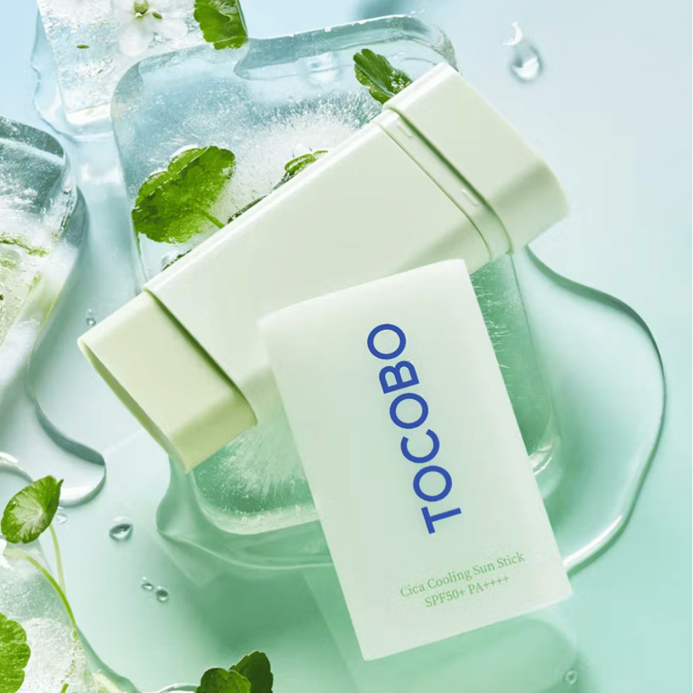 Tocobo Cica Cooling Sun Stick SPF50+ PA++++ på isterninger med grønne planteblade, hvilket giver en kølende og forfriskende følelse.