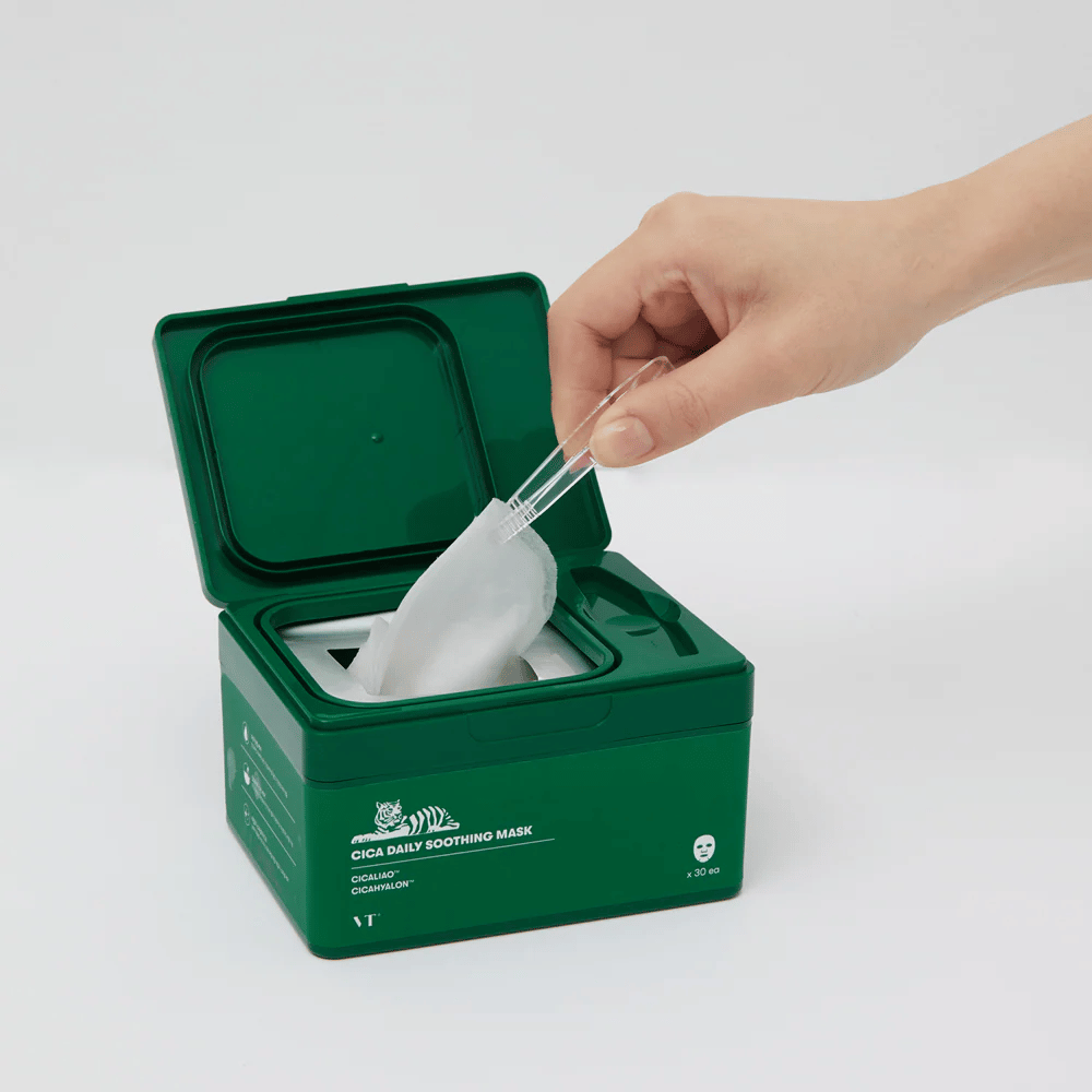 Hånd anvender en pincet til at tage en Sheet mask op fra en grøn beholder mærket "Cica Daily Soothing Mask".