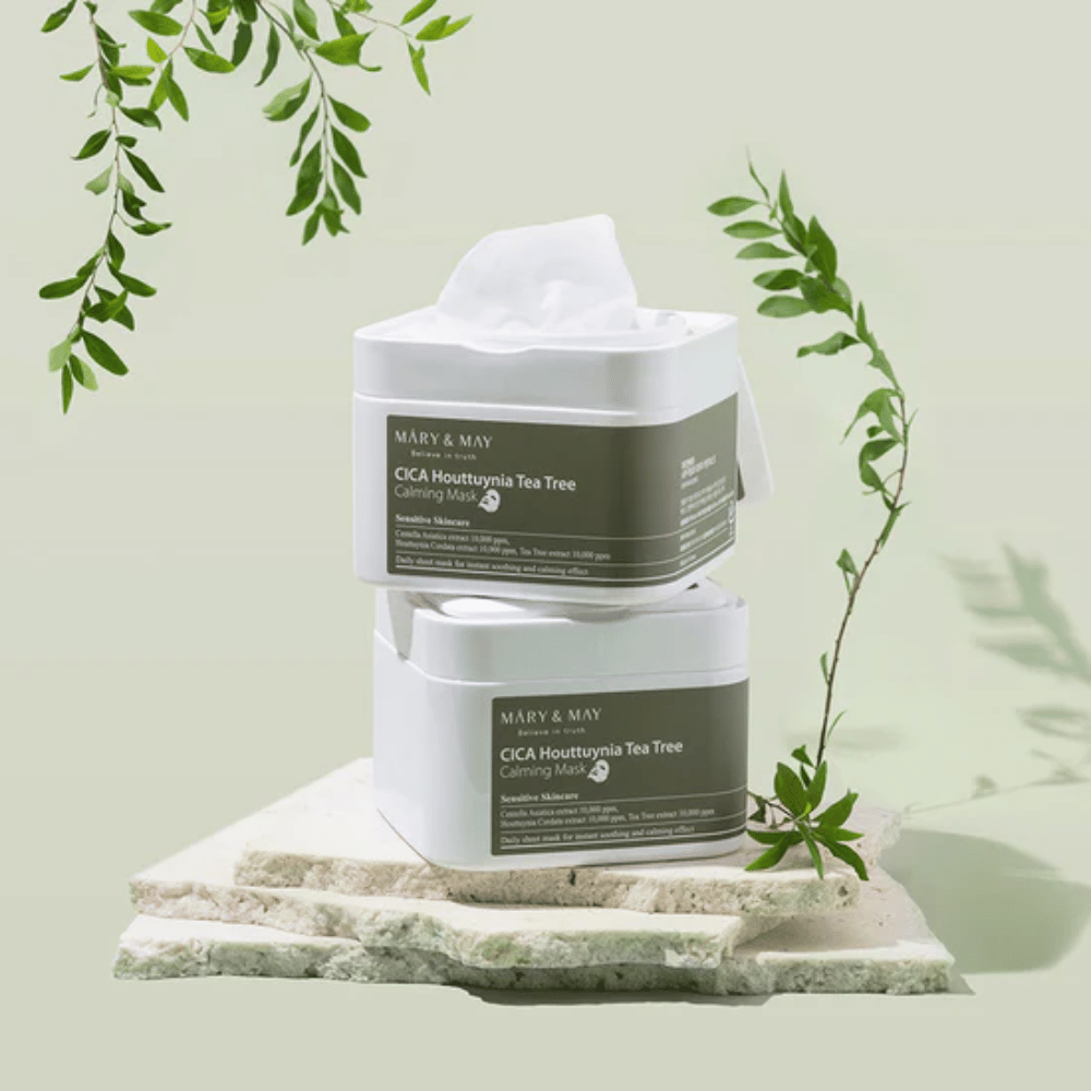 To krukker Mary & May Cica Houttuynia Tea Tree Calming Mask placeret på natursten med grønne plantedele – beroligende sheetmasker til sensitiv hud.