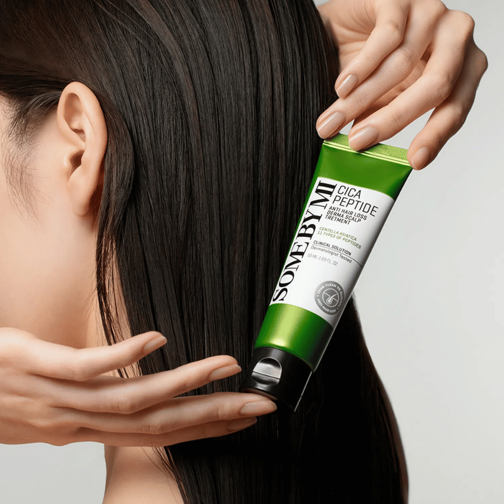 Kvinde anvender SOME BY MI Cica Peptide Anti Hair Loss Derma Scalp Treatment i langt, mørkt hår med en grøn og hvid tube.